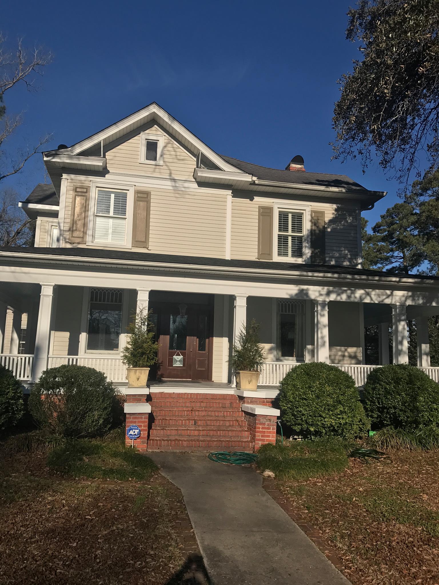 Two-story tan home with white wrap-around porch